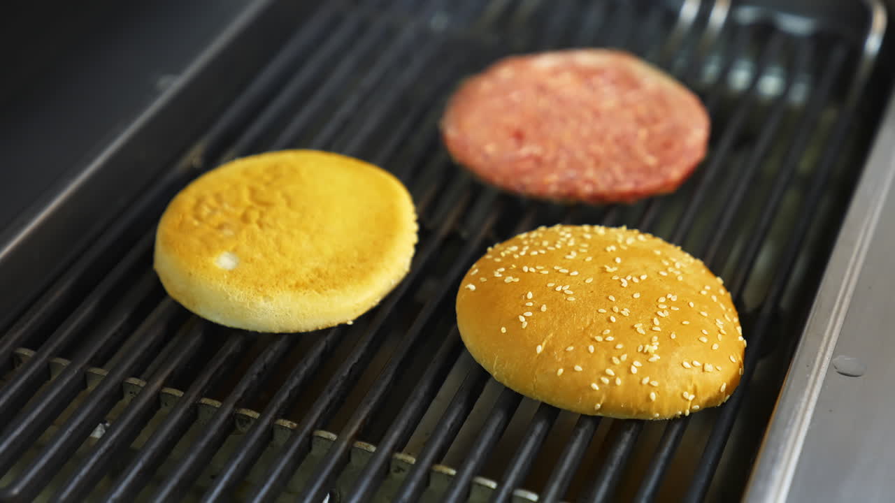 Cooking beef and pork patty for burger. Meat roasted with buns at kitchen grill. Selective video from above.