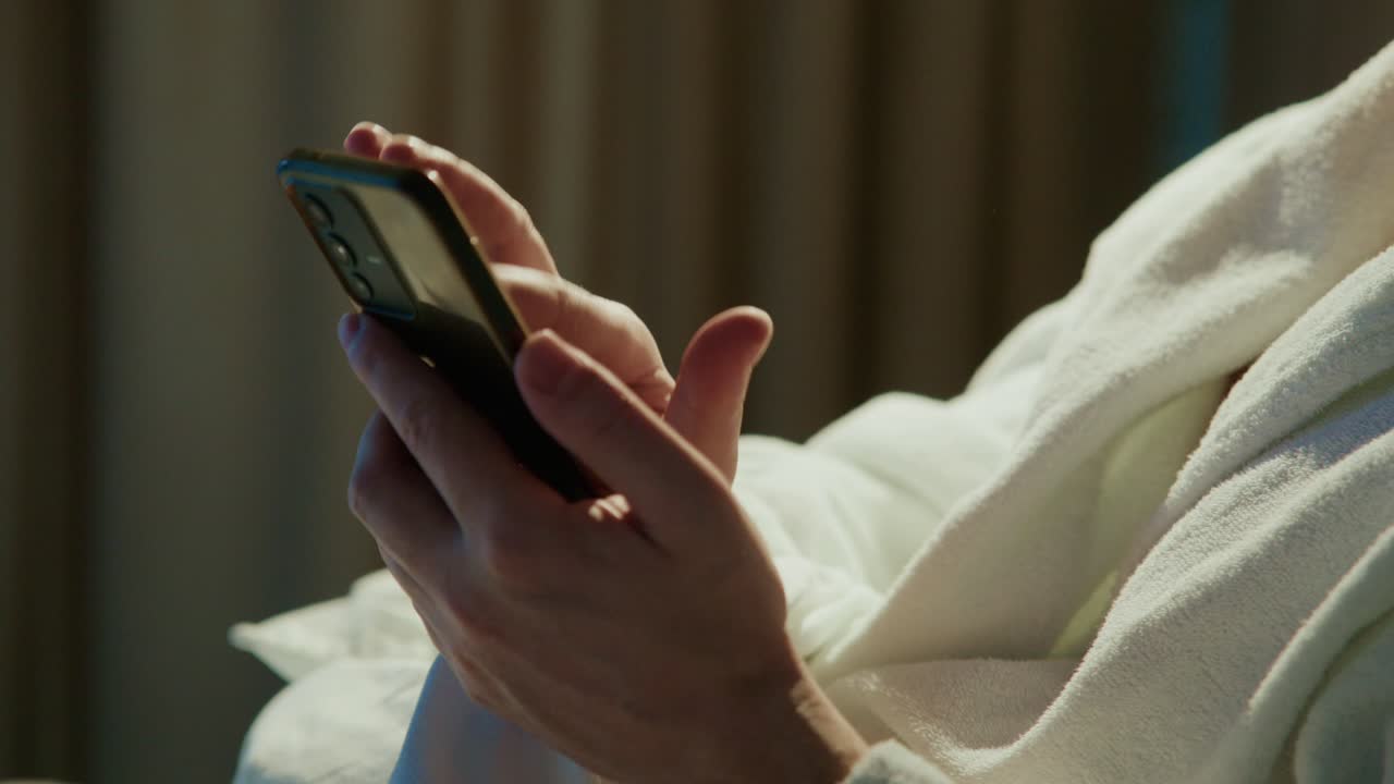 In un ambiente tranquillo, una persona si gode una serata rilassante indossando un accappatoio comodo, mentre utilizza uno smartphone con attenzione. Un'illuminazione soffusa contribuisce a creare un'atmosfera accogliente.