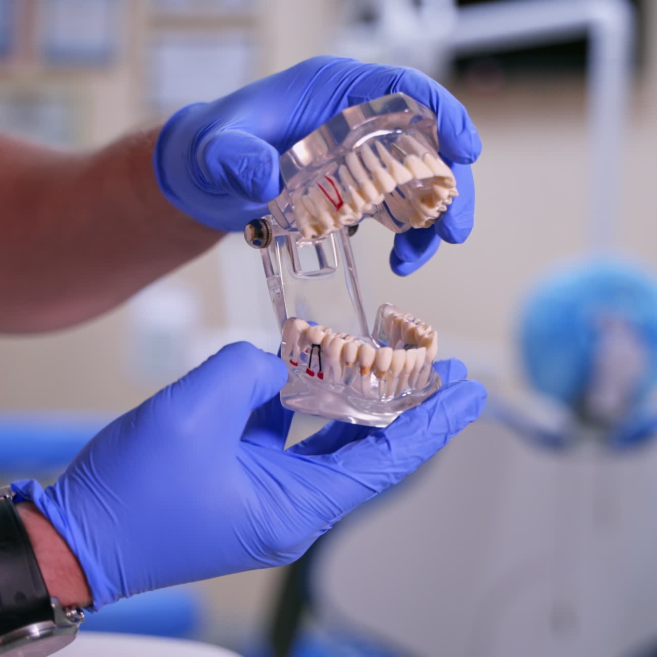 Doctor shows on a plastic jaw sample or model different methods of teeth treatment. Modern dental clinic background. Blue medical gloves on male doctor's hands. Dental Hygiene and Health concept video.