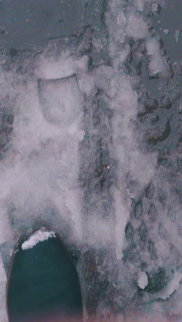 man feet in black leather boots walk fast along asphalt road with melted snow and slush close first point view