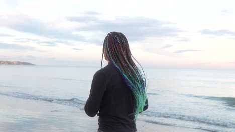 mujer con trenzas corriendo en la playa con el mar en el fondo