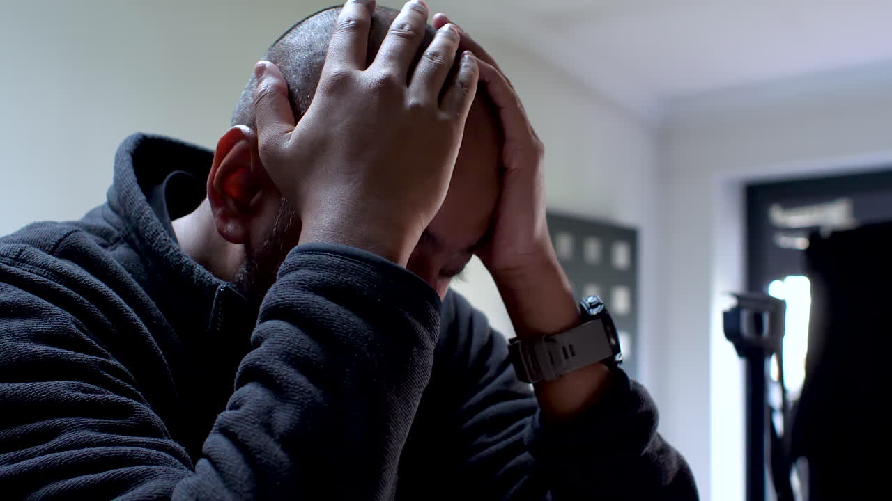 British Asian Male sits with his rubbing his hands across his face, his expression fraught with the weight of burdens, vividly capturing the palpable strain of stress and anxiety