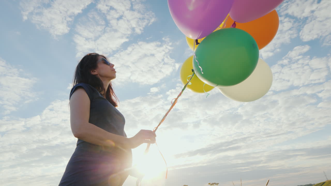 mujer embarazada feliz jugando con globos contra el cielo azul