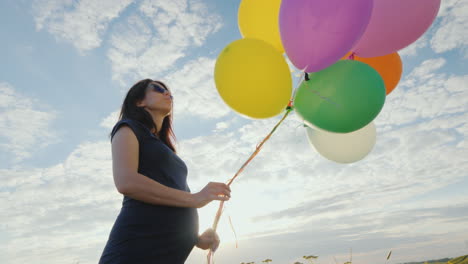 happy pregnant woman playing with balloons against the blue sky