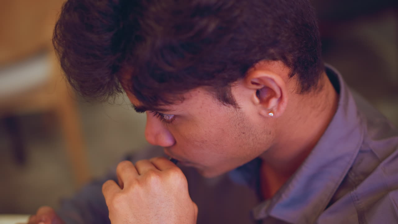 Close-up side view of young man with head slightly down, eyes closed, wearing stud earring and formal shirt, in soft lighting, conveying mood of contemplation, fatigue, or peaceful rest in quiet indoor space