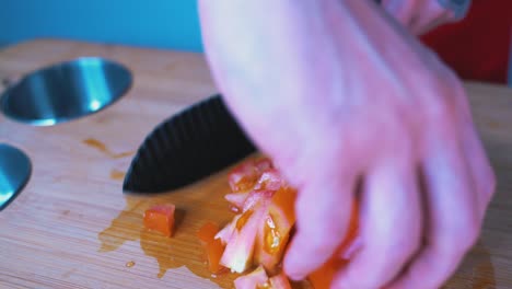 chef chopping a tomato on a chopping block, close up on hands, and black knife