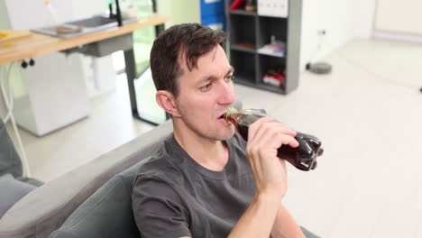 Man drinking soda from a bottle while relaxing on a couch at home