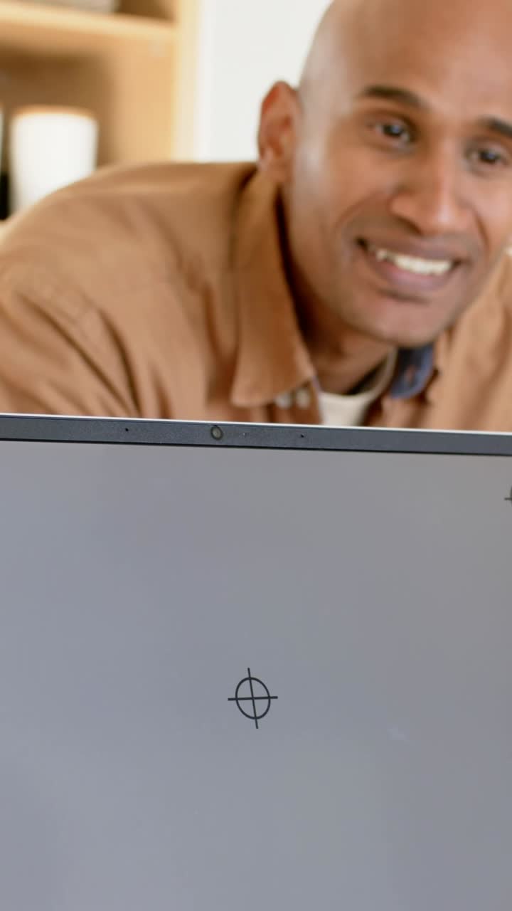 Vídeo vertical: Homem debruçado olhando para laptop em casa, notando mira, sorrindo com camisa marrom.