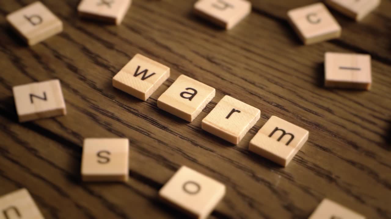 Wooden letter tiles spell the word warm as the camera pans across a wooden surface with cozy lighting.