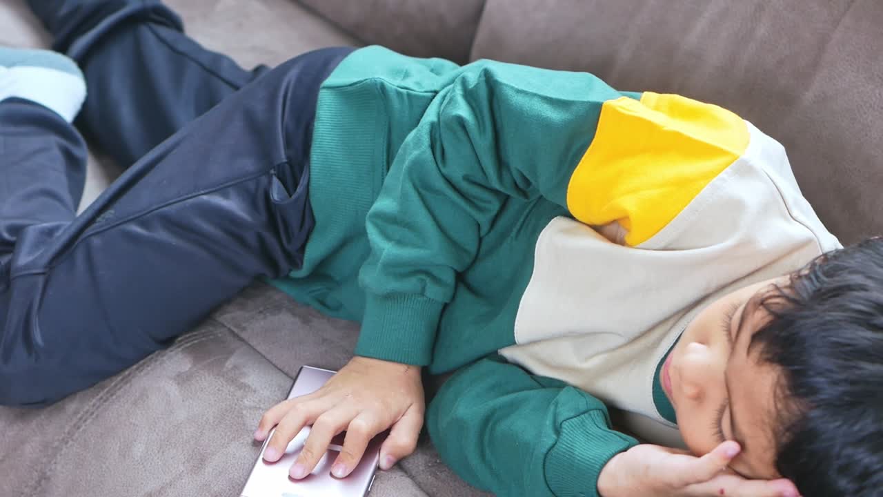 Tired child napping on sofa with phone nearby