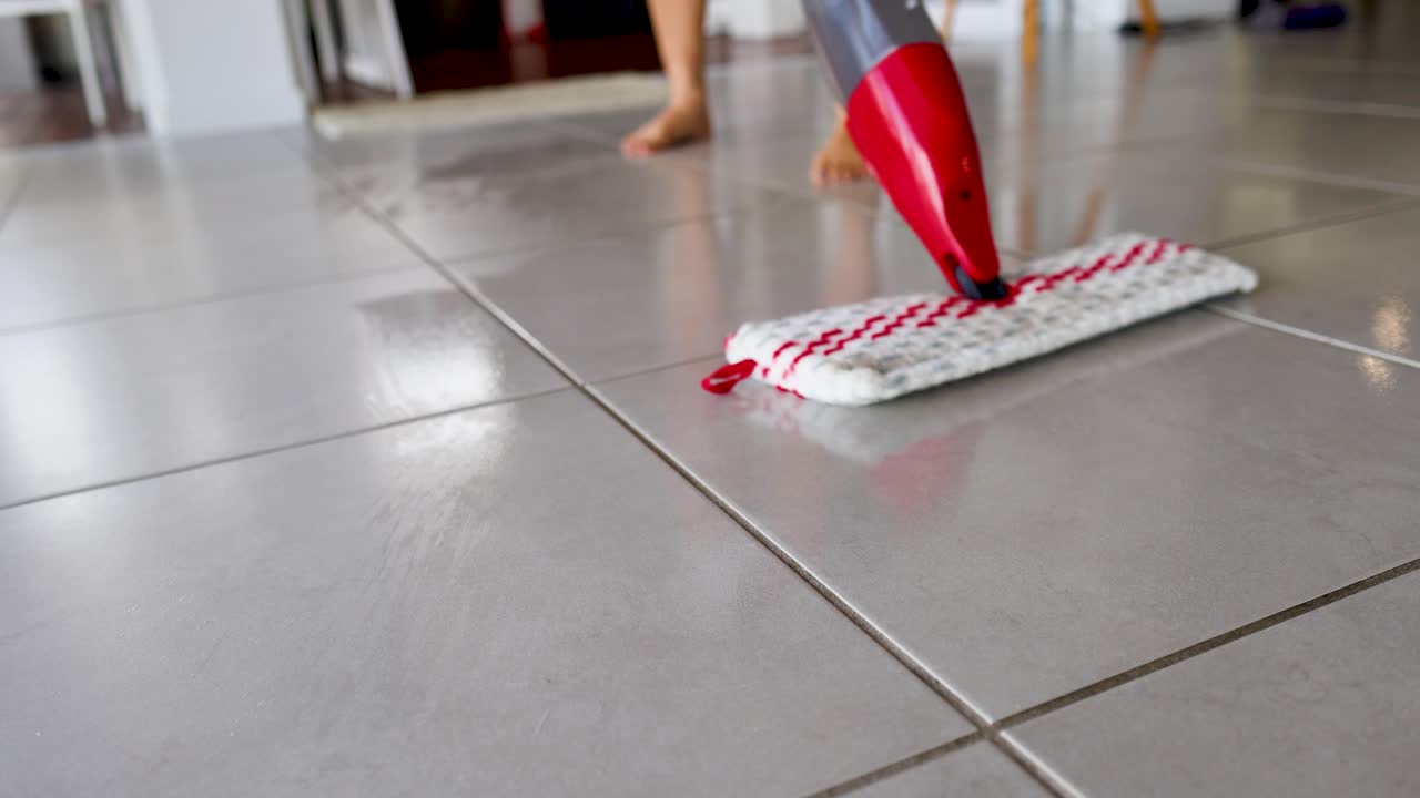 A red spray mop glides over tiled floor, cleaning efficiently in a bright, indoor setting
