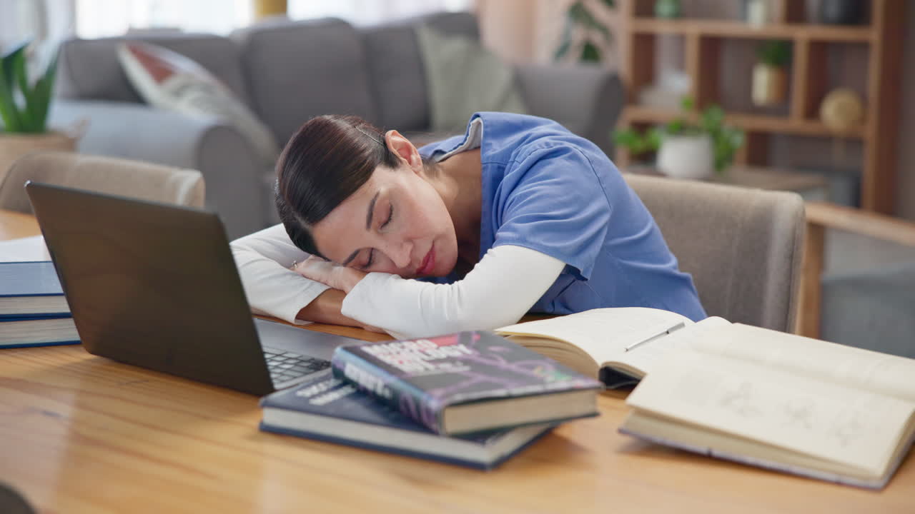 Infermiera esausta che dorme alla scrivania con libri e laptop