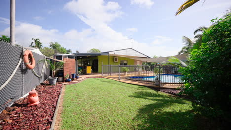 pullback on grassy tropical lawn of colourful home backyard with lush garden and fenced pool