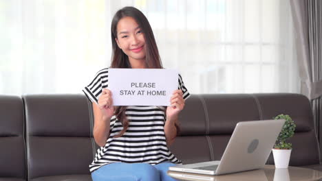 thai woman holding stay at home paper page in room interior, social distancing covid-19 campaign