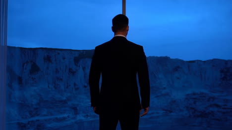 man in suit gazing at dramatic blue landscape from window