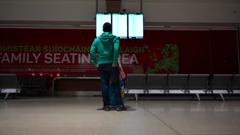 hombre turista con un equipaje comprobando el panel de pantalla de los vuelos para encontrar su puerta de embarque en el aeropuerto
