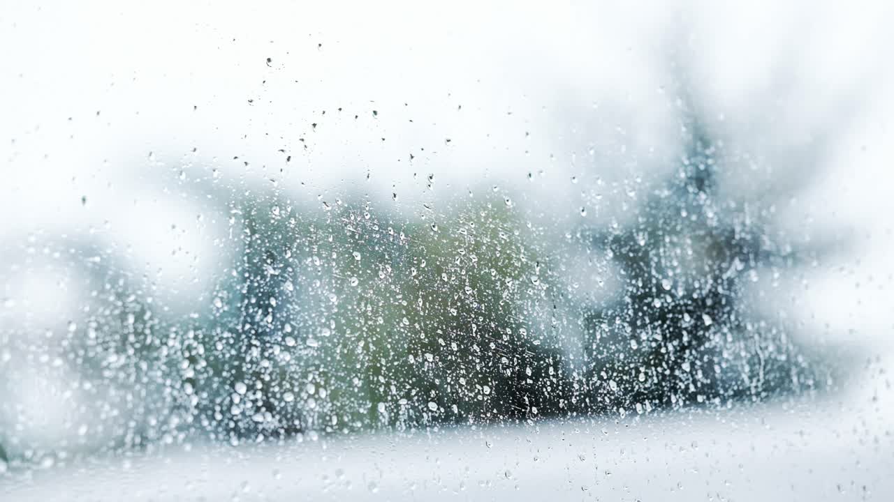 Rain drops against a glass window with trees out of focus in the distance