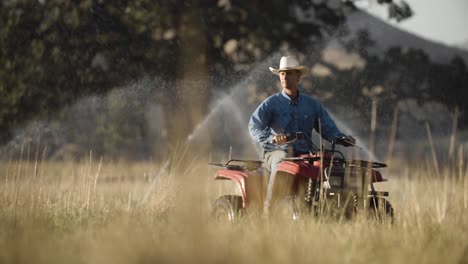 ranchero montando un atv a través de su campo que está siendo regado