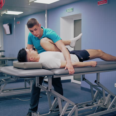 physiotherapist is leaning and stretching patient's leg a medical center. young masseur is giving leg treatment to a client lying on a massage table. physical therapy concept.