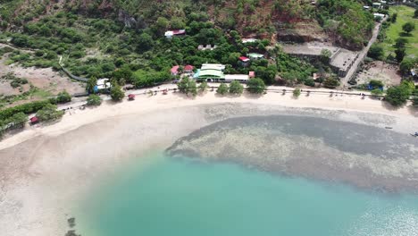 Aerial-static-drone-of-motorbike-cruising-along-the-coastal-road-on-tropical-island-Timor-Leste,-South-East-Asia