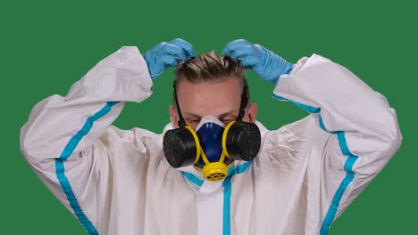 portrait of a male doctor in a white protective suit and surgical gloves looking at the camera puts on a medical respirator and safety glasses. green screen, chroma key. slow motion. close up