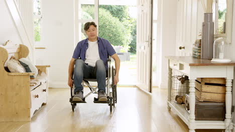 mature asian man in wheelchair pushing himself in hallway at home towards camera- shot in slow motion