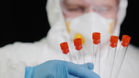 A-man-in-protective-clothing-and-a-respirator-holds-several-test-tubes