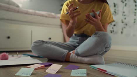 zoom in of caucasian teenage girl sitting on floor and making notes on flash cards