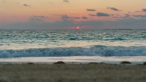 ocean waves gently rolling to shore at sunset with vibrant horizon