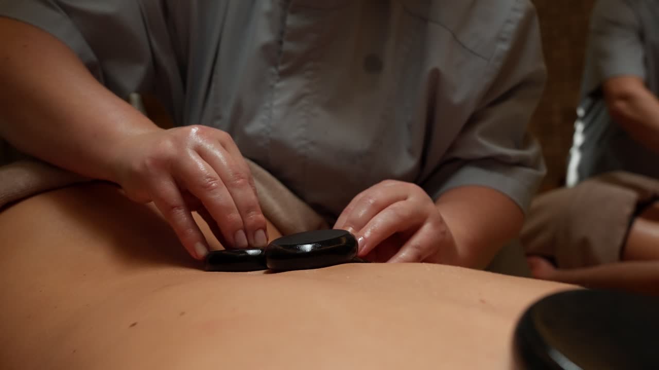 Massør placerer varme sten på en persons ryg under spa-behandling