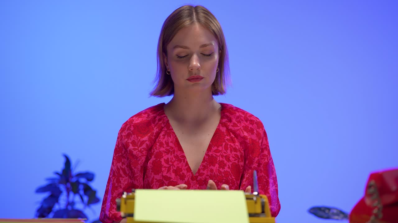 A young woman in a red floral dress types thoughtfully on a bright yellow vintage typewriter. Set against a clean blue background, this vibrant scene captures retro office charm and creative focus