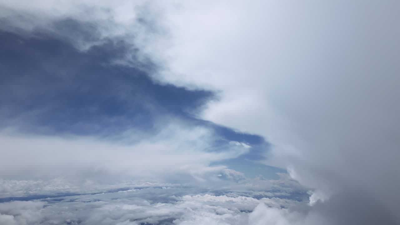 An immersive view through the pilot’s eyes from a jet cockpit while flying near the top of a huge cumulonimbus storm cloud under an intense blue color sky.