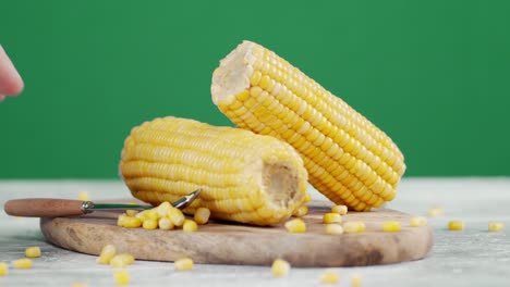 male hand puts the spoon with grains of corn on the wooden cutting board.