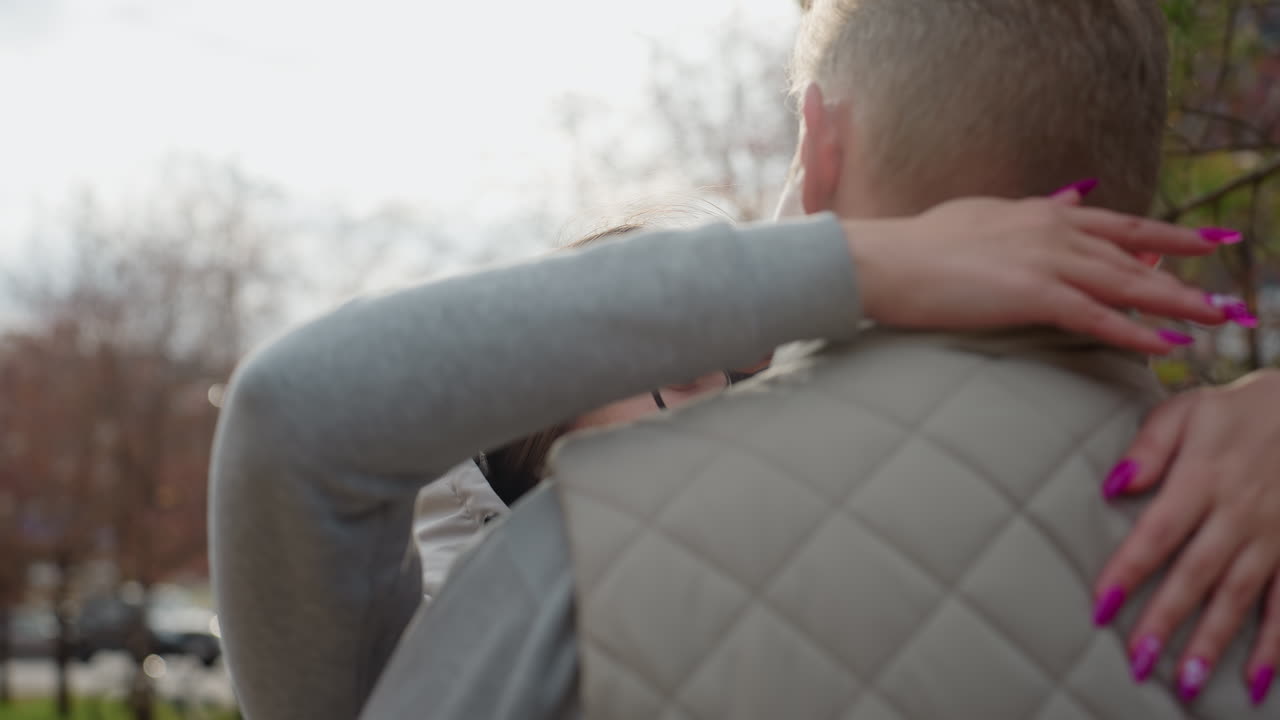 Close up of smiling woman in glasses walking toward brother for warm hug outdoors with soft breeze swaying her hair surrounded by autumn trees and city buildings in gentle morning sunlight
