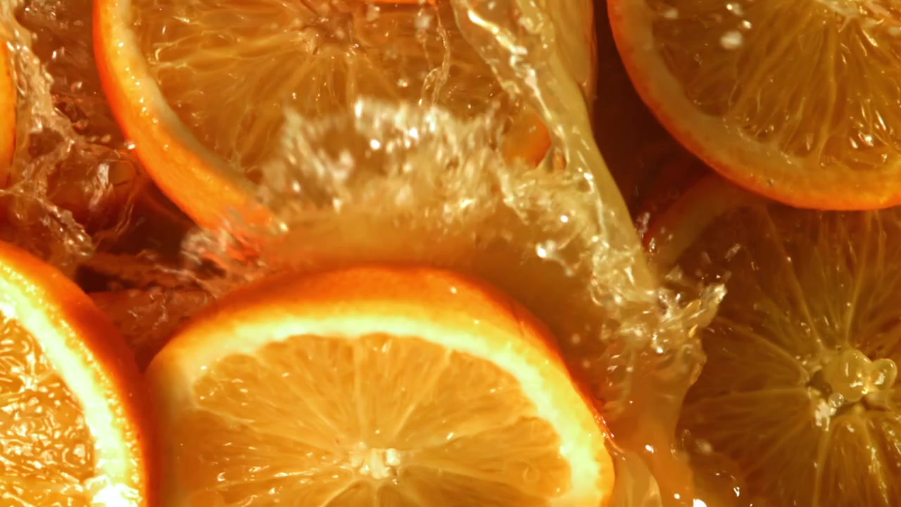 Friske appelsinskiver som spruter ned i gylden juice i sakte film