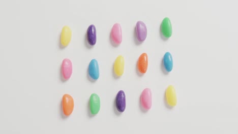 video of overhead view of rows of multi coloured sweets over white background