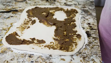 spreading out the cinnamon and brown sugar and butter mixture on rolled dough to make cinnamon buns