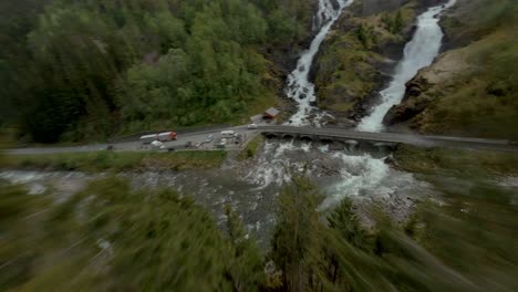 Luft-FPV-Flug-Bergab-Grüne-Berge-über-Straße-Mit-Verkehr-Und-Wasserfall-In-Norwegen,-Låtefoss