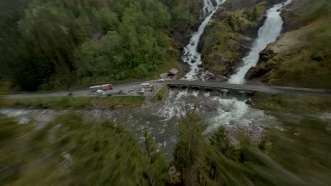 aerial fpv flight downhill green mountains over road with traffic and waterfall in norway,lã¥tefoss