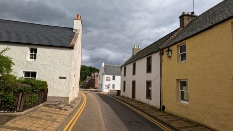 A steady daytime walk down a quiet Cromarty street, lined with pastel traditional houses under overcast skies, captured in smooth forward camera movement
