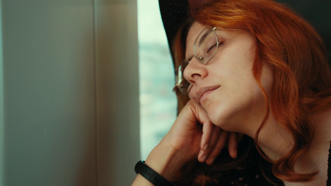 Donna dai capelli rossi che dorme su un treno, sdraiata sul sedile