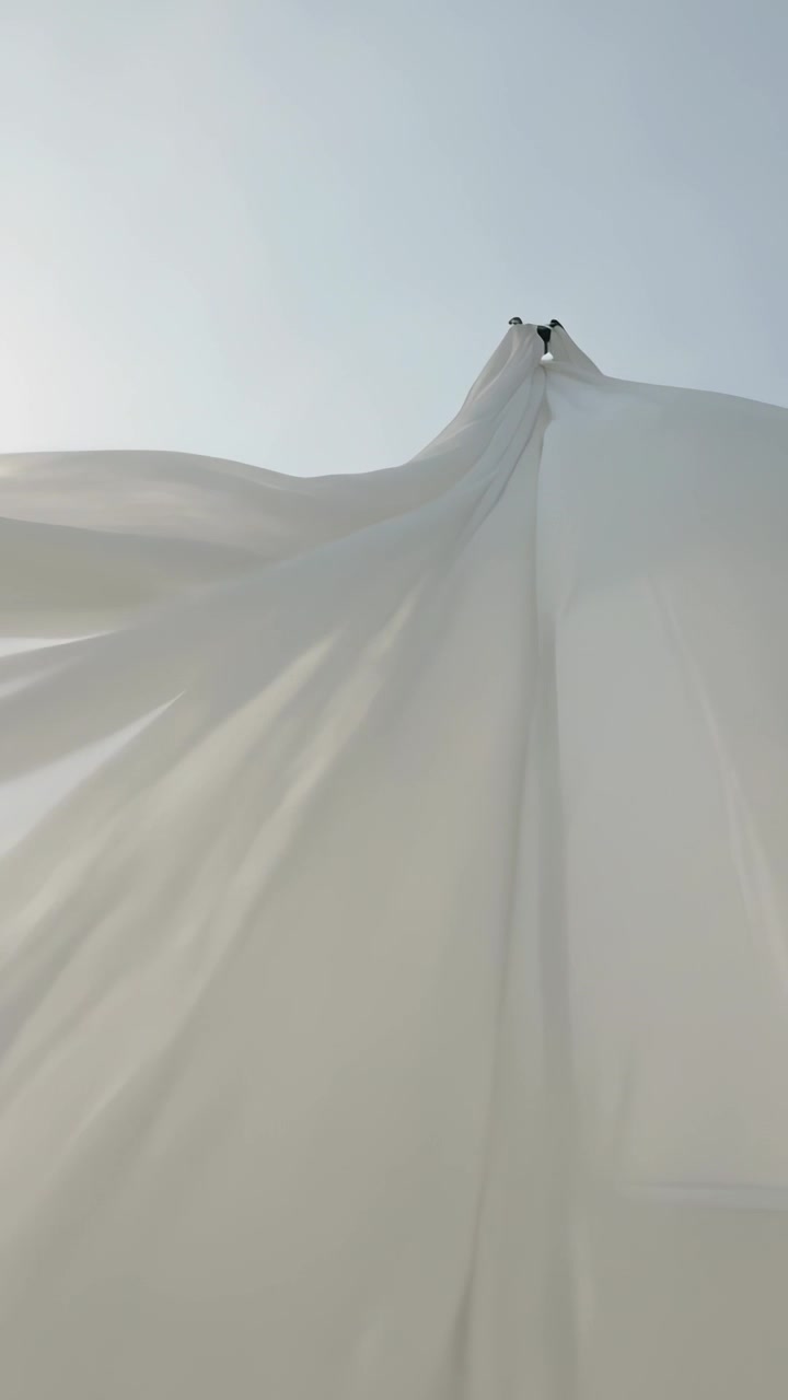 Vertical video: Breeze rising, white sheet billowing, forming folds against sky with two anchors