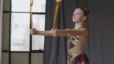 young girl in leotard practising rhythmic gymnastics with clubs in a studio 5