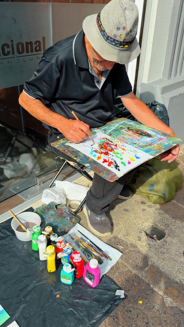 ซานโฮเซ คอสตาริกา 7 สิงหาคม 2025: ศิลปินข้างถนนกำลังวาดภาพบนทางเท้า ซานโฮเซ คอสตาริกา มุมมองจากที่สูงของผู้ชายคนหนึ่งพร้อมผ้าใบ พู่กัน และสีอะคริลิกบนทางเท้า