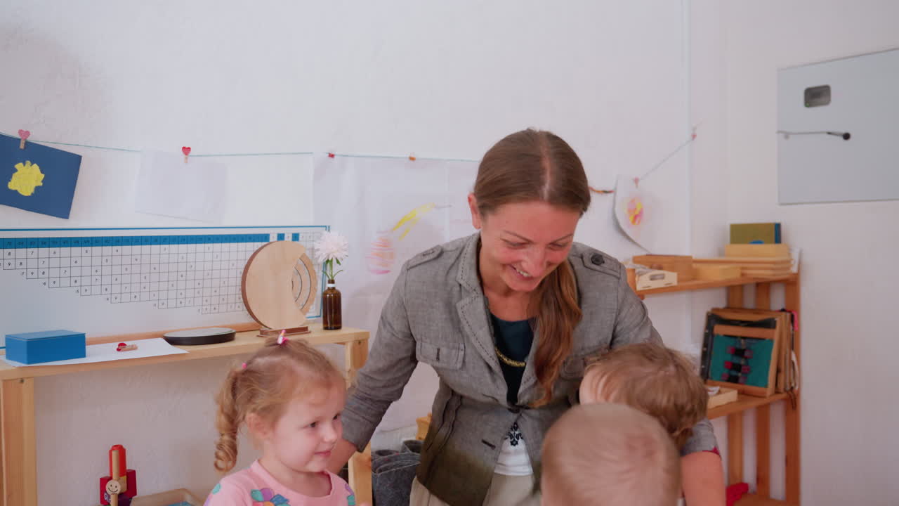 Smiling teacher embraces small children in cheerful classroom surrounded by shelves, drawings, and learning materials, expressing affection, care, and connection during joyful preschool