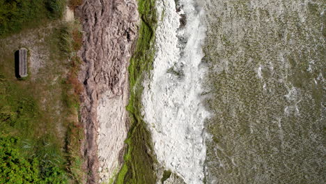 Aerial-top-down-shot-of-waves-of-Baltic-sea-reaching-green-coastline-on-Hel-Island-during-sunny-day