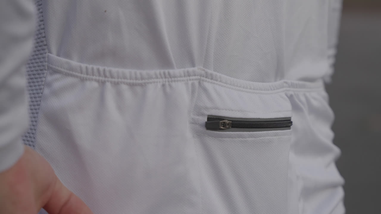 Primer plano de ciclista masculino guardando el teléfono móvil en el bolsillo trasero del maillot, mostrando equipamiento de ciclismo práctico y una rutina de entrenamiento al aire libre.