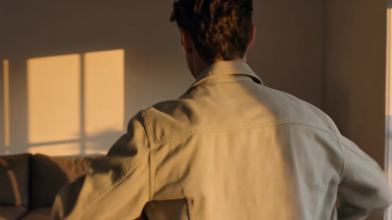 Reaching adult male prompted by warm sunlight lifting beige jacket onto shoulders in living room