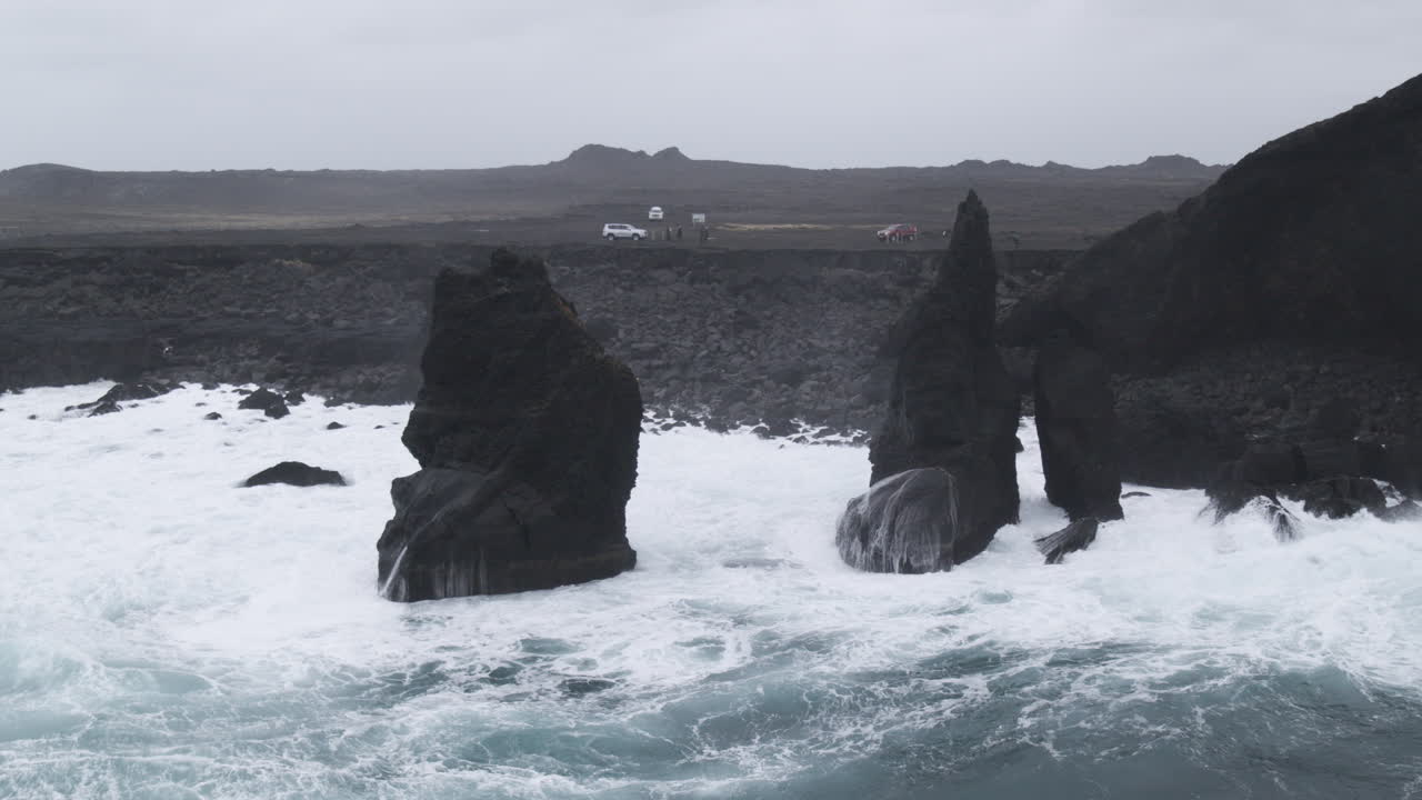 fotografía aérea de las olas de la costa de islandia a través de los acantilados y la gente mirando el horizonte en un día de niebla