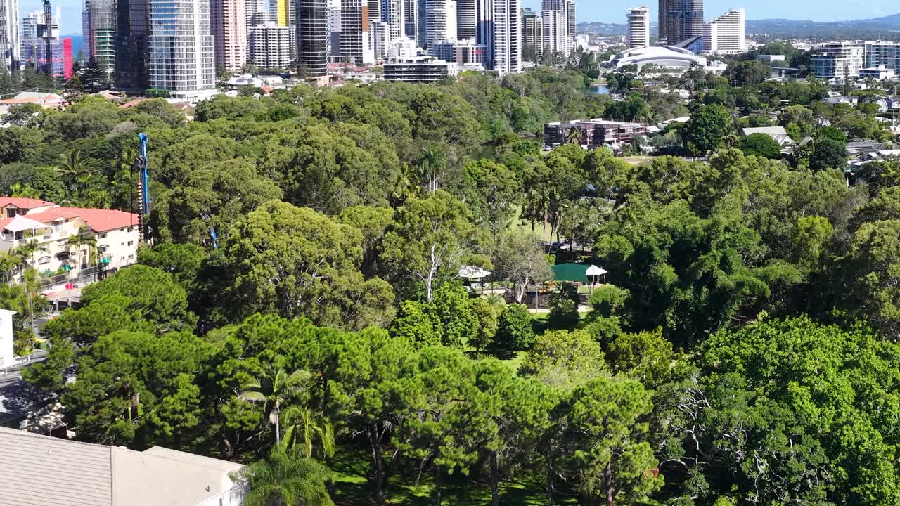 高所からのドローン撮影で、緑豊かな公園を横切るようにパンしながらゴールドコーストの街のスカイラインへ向かう。
